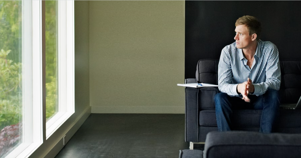Man sitting in chair with hands in lap while looking out of window.