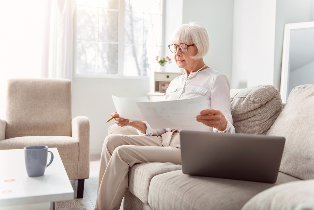 Older lady sitting on couch reading about retirement planing and social security. 