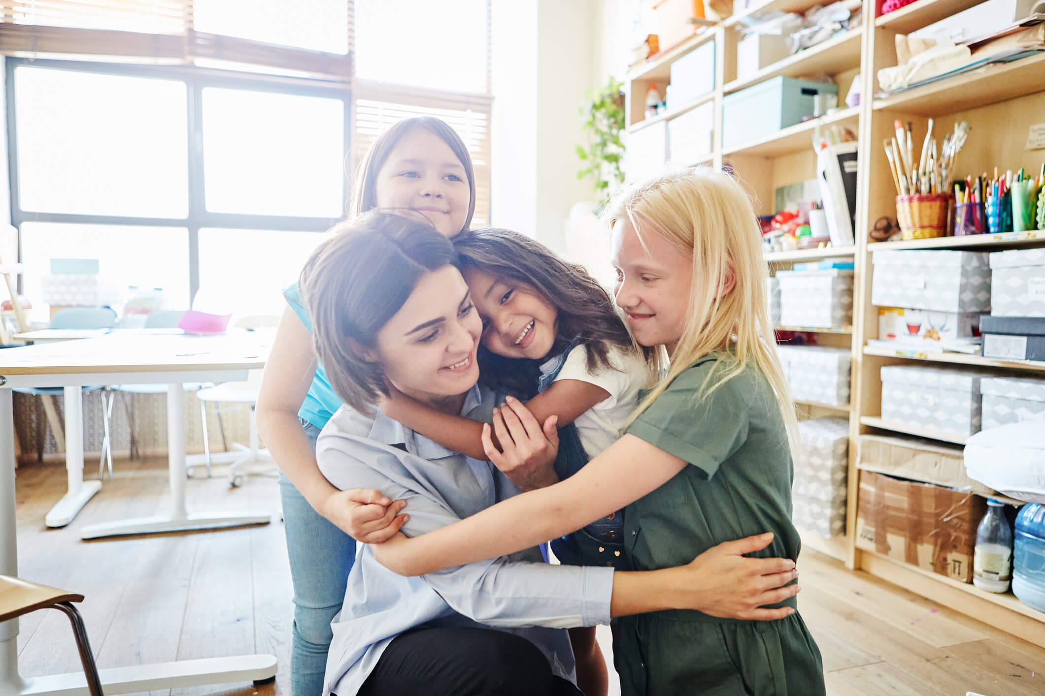 cute-girls-smiling-and-embracing-tenderly-their-teacher-in-a-classroom